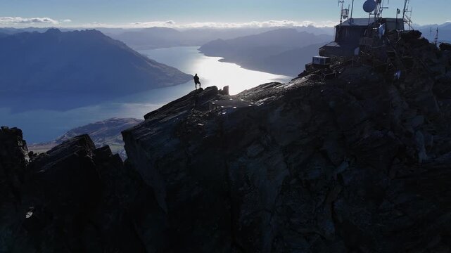 High contrast aerial silhouette: Man on summit above lake, Queenstown