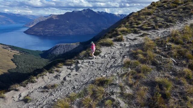 Lone hiker descends rugged mountain trail high above Lake Wakatipu, NZ