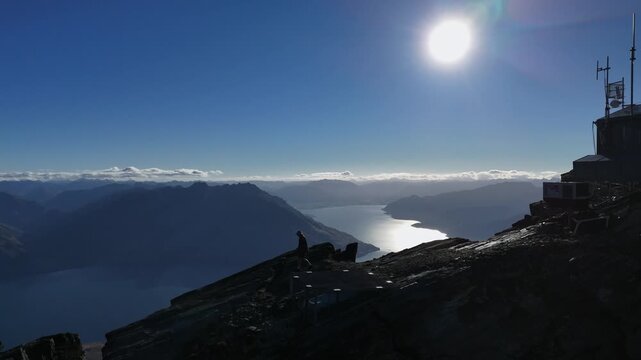 Lone person by mtn peak telecom tower, silhouette above silvery lake