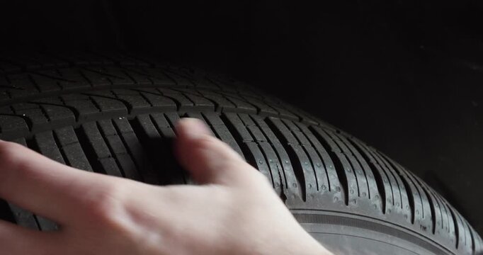 Close-up of a hand checking tire tread depth on a car wheel. Concept of vehicle maintenance, safety inspection and driving preparation.