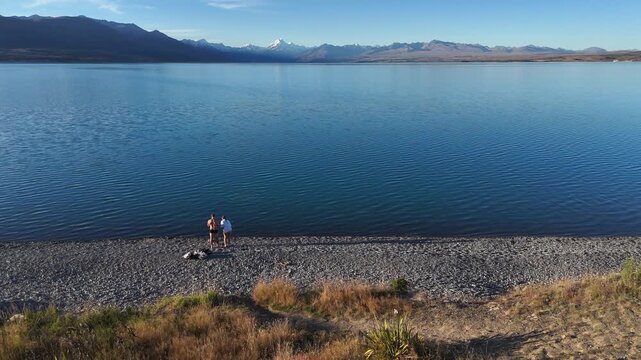 Tourists toss stones into Lake Pukaki with Mount Cook in background
