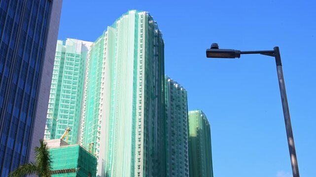 Modern apartment complex facade draped in construction safety nets during a sunny day. The shot illustrates the dense housing infrastructure and ongoing vertical development of the metropolis.