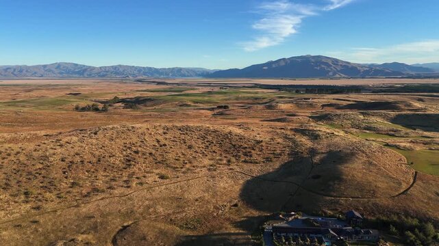 Flyover farmhouse on rolling golden mountain plateau, blue sky horizon
