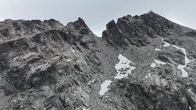 Aerial rises up jagged monochromatic mountain rock toward summit