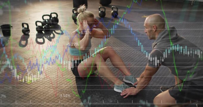 Female trainee doing crunches for core, trainer bracing feet and cueing, finance charts overlaying