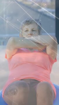 Vertical video: Woman doing crunches on blue ball while camera pulling back, HUD tracking fitness