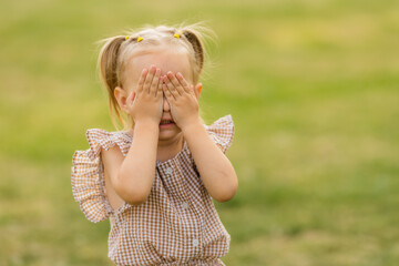 Obraz premium a portrait of a little blonde girl covered her face with her hands in the summer