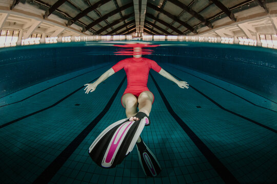 Woman swimming underwater in red swimsuit with flippers split shot view in a modern indoor pool