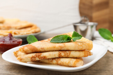Tasty crepes with mint leaves and jam served on wooden table, closeup © New Africa