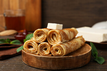 Tasty rolled crepes with butter and mint leaves served on wooden table, closeup © New Africa