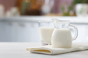 Fototapeta premium Fresh milk in glass and jug on white wooden table indoors, closeup. Space for text