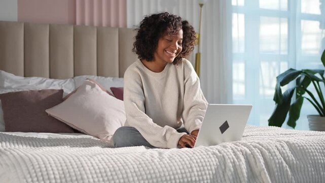 African American girl using laptop in bed at home office typing chatting reading writing email. Young black woman having virtual meeting online chat video call conference. Work learning from home