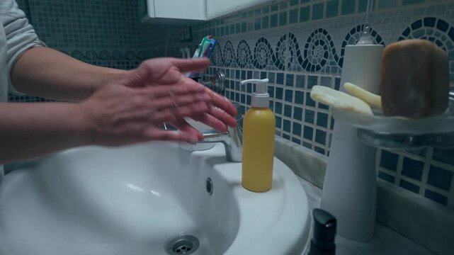 Daily routine of a woman washing hands at a tiled bathroom sink with liquid soap, emphasizing hygiene, self-care, cleanliness and personal grooming in a home bathroom setting.