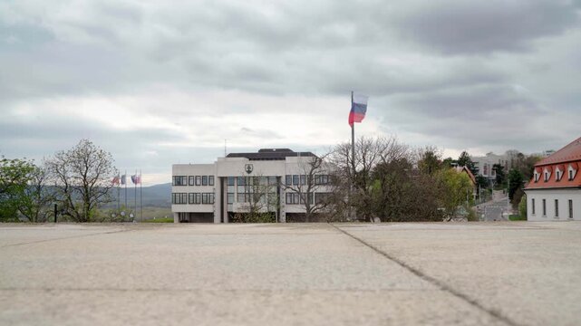 Exterior of National Council of the Slovak Republic building in Bratislava with waving Slovakian flag. National flag of Slovakia flies in front of Narodna Rada parliament on cloudy spring day. 4K