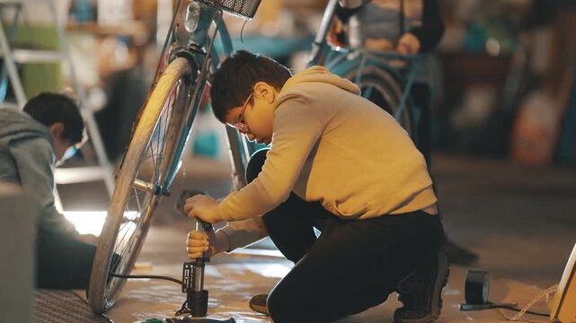 Young boy inflating a bicycle tire with a pump in a garage