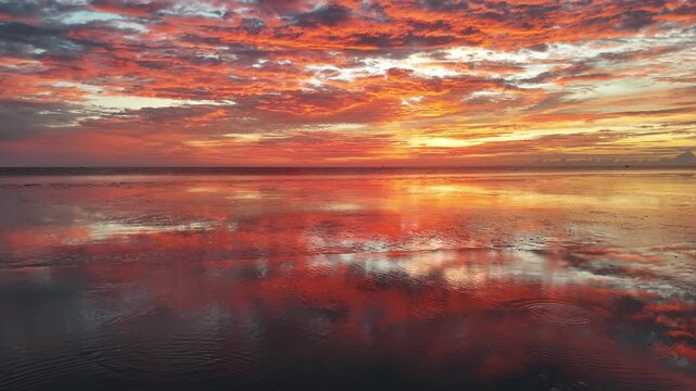 Aerial shot shows muddy coastal landscape with glowing sunset horizon and shimmering tidal waters.
