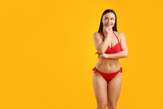 Beautiful woman in stylish swimsuit posing on yellow background. Space for text