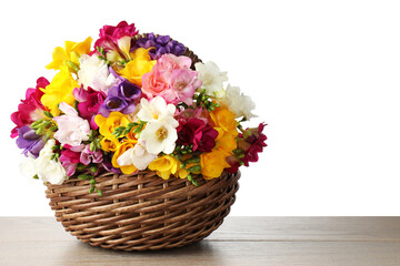 Obraz premium Beautiful freesia flowers in wicker basket on wooden table against white background