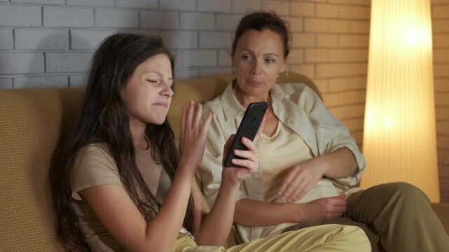 Internet addiction, lack of communication. Teenage daughter ignoring her mother while engrossed in her smartphone, mother texts her on her phone