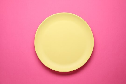 Empty plate on pink background, top view