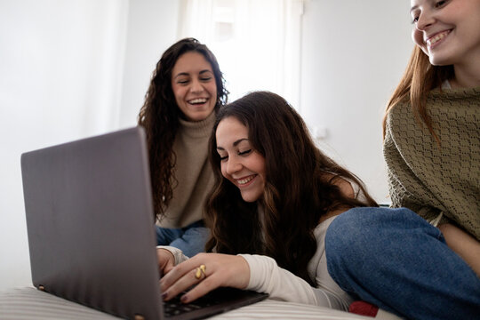Happy friends laughing together while using a laptop at home