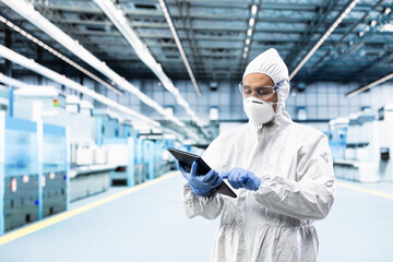 Indian technician in microchip factory testing silicon wafer batches with tablet control app. Tech expert monitoring semiconductor manufacturing plant machinery readouts with device © DC Studio