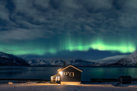 Northern lights over a cabin by Tromso fjord, Norway