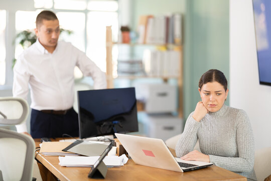 Young businessman of a large company, scolds his employee girl sitting at workdesk in the office