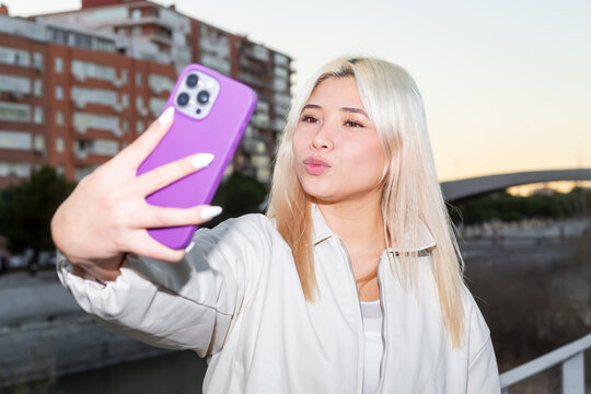 Gen Z girl taking selfie with smartphone in city at dusk