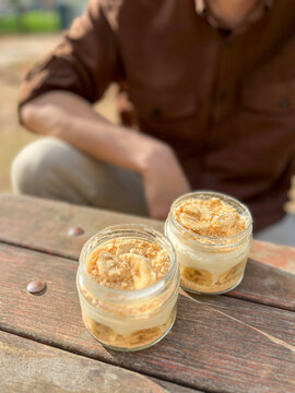 Two glass jars of banana pudding with crumbs on a rustic table