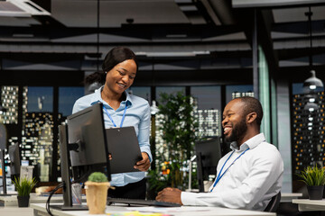 Fototapeta premium African american staff members consulting each other for monthly reports, reviewing KPI data insights for business productivity late at night. Collaboration between employees for success.
