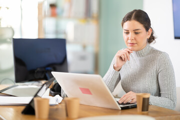 Fototapeta premium Young woman at her desk in modern office and working on laptop