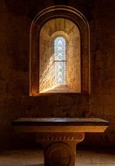 Le Thoronet Abbey interior, Provence-Alpes-Côte d’Azur, France : Romanesque window with sunlight illuminating stone altar in monastery