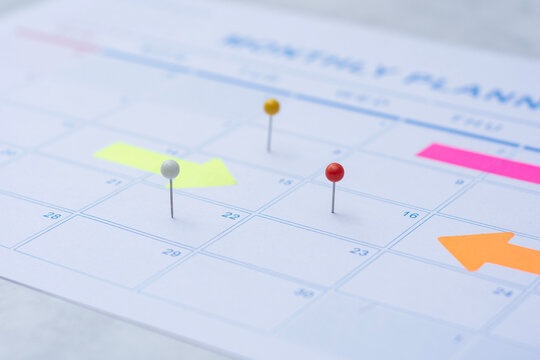 Close up of a monthly wall calendar featuring push pins and bright arrow post-it notes to mark important dates. Concept project management, financial planning, and organized workflow.