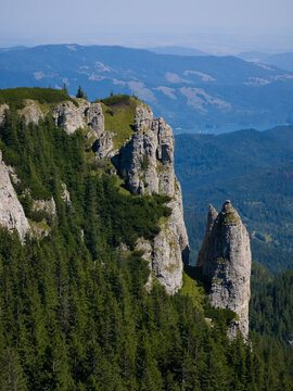 Claile Miron rock towers rising along steep cliffs and evergreen coniferous forest above distant mountain valleys under a clear blue sky on Ceahlău Massif, Romania.