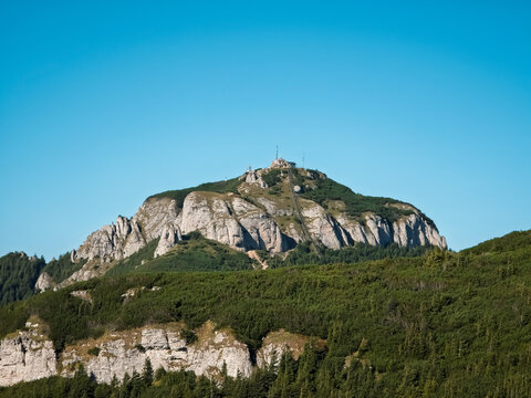 Toaca Peak (V&acirc;rful Toaca) featuring its iconic staircase and meteorological station rising above rocky cliffs and alpine vegetation under a clear blue sky on Ceahlău Massif, Romania.