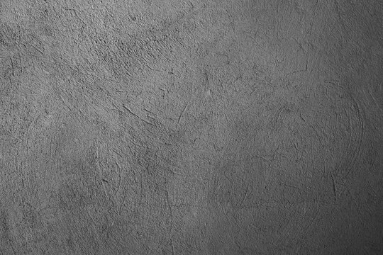 Rough industrial cement wall showcasing a monochromatic grey palette with web like cracks and aged, chipping plaster like textures dark with texture gray background on rough concrete surface backdrop