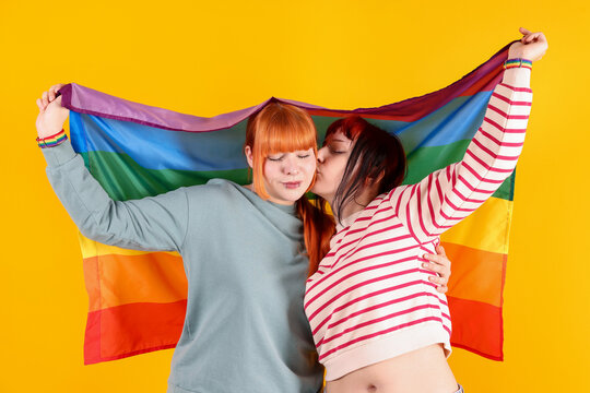 Lovely lesbian couple with rainbow flag on yellow background. LGBT concept