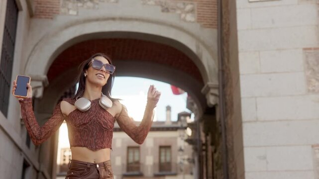 Stylish young woman dancing and listening to music in the city