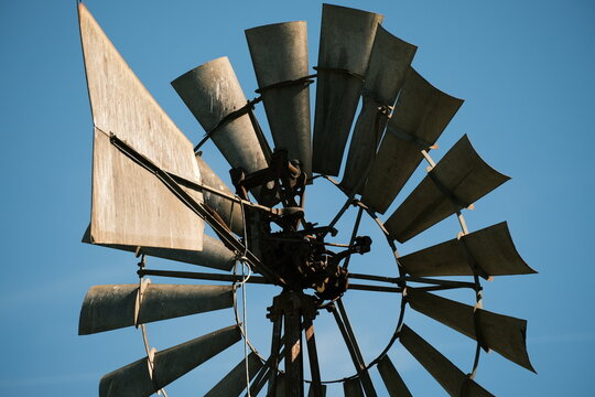 Close-up of a vintage rusted metal wind pump wheel and blades against a clear blue sky.