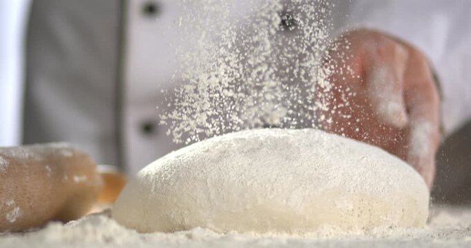 Super Slow motion chef sprinkling flour over ready dough
