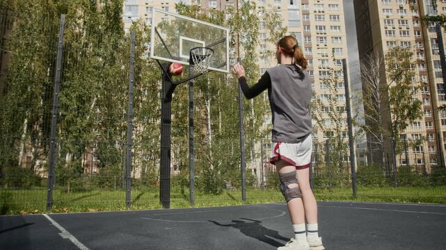 Full length shot of athletic teenage girl playing basketball alone on sunlit urban outdoor court taking free throw missing hoop, youth sports concept, copy space