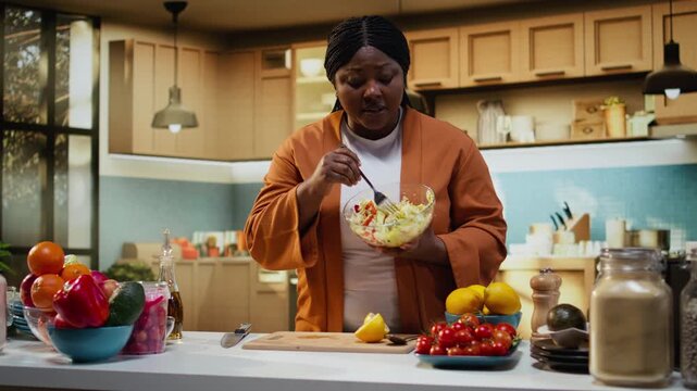 Black food vlogger mixing vegetables for a salad recipe in bowl, creating lifestyle cooking video in the kitchen. Home chef organizing ingredients on the counter, recipe tutorial and meal prep.