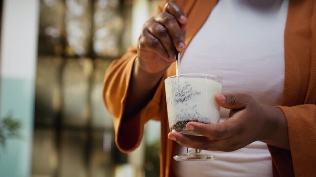 Female food influencer mixing chia pudding ingredients in a bowl, filming morning kitchen routine for a healthy breakfast idea. Chef preparing nutritious chia seeds and yogurt, lifestyle content.