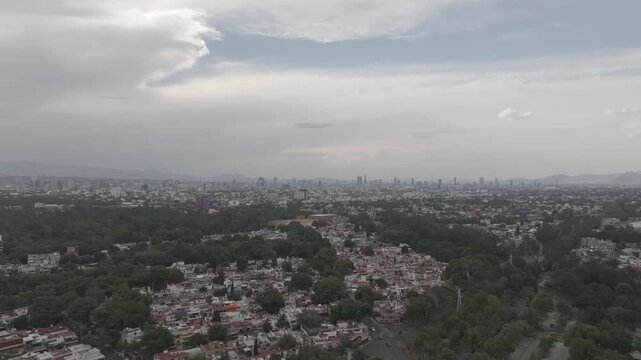 Aerial drone flying sideways over Coyoac&aacute;n with distant Paseo de la Reforma skyline and overcast sky in M&eacute;xico City. Shot in D-Log M