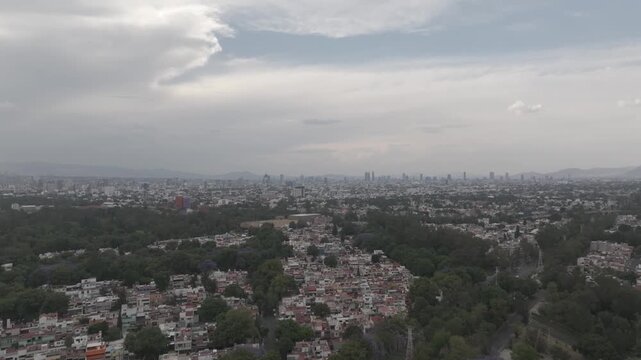 Aerial drone flying forward over Coyoac&aacute;n with distant Paseo de la Reforma skyline and overcast sky in M&eacute;xico City. Shot in D-Log M