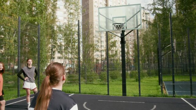 Dynamic tilt up shot of teenage girl dribbling ball and shooting free throw missing hoop while playing basketball on urban outdoor court with team watching, copy spac