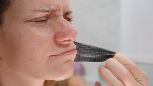 Woman Pulling Black Hostage Tape Breathable Mouth Tape from Lips Showing Pained Expression in Close-Up View for Sleep Wellness Concept