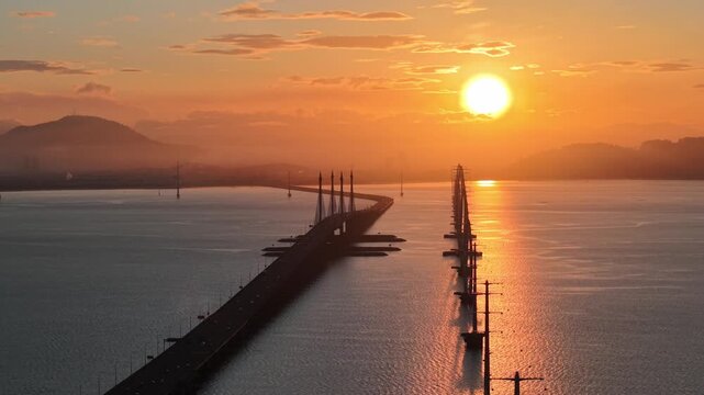 Aerial sunrise view shows Penang Bridge stretching across calm waters and TNB transmission towers.