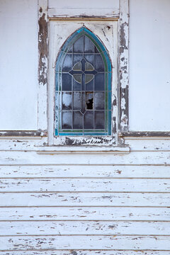 Close-up of a dilapidated church arched window with broken panes and peeling paint